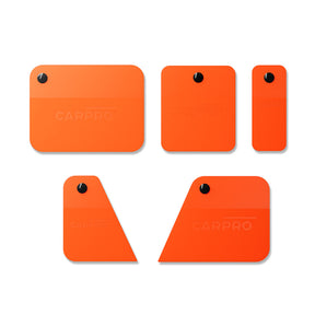 cinque spatole arancioni di diverse forme e dimensioni del CARPRO Immortal Squeegee Kit. Ogni spatola ha un foro nero per appenderla e il logo CARPRO inciso su di esse. Queste spatole sono progettate per un'applicazione precisa delle pellicole protettive, assicurando risultati professionali senza bolle.   3/3